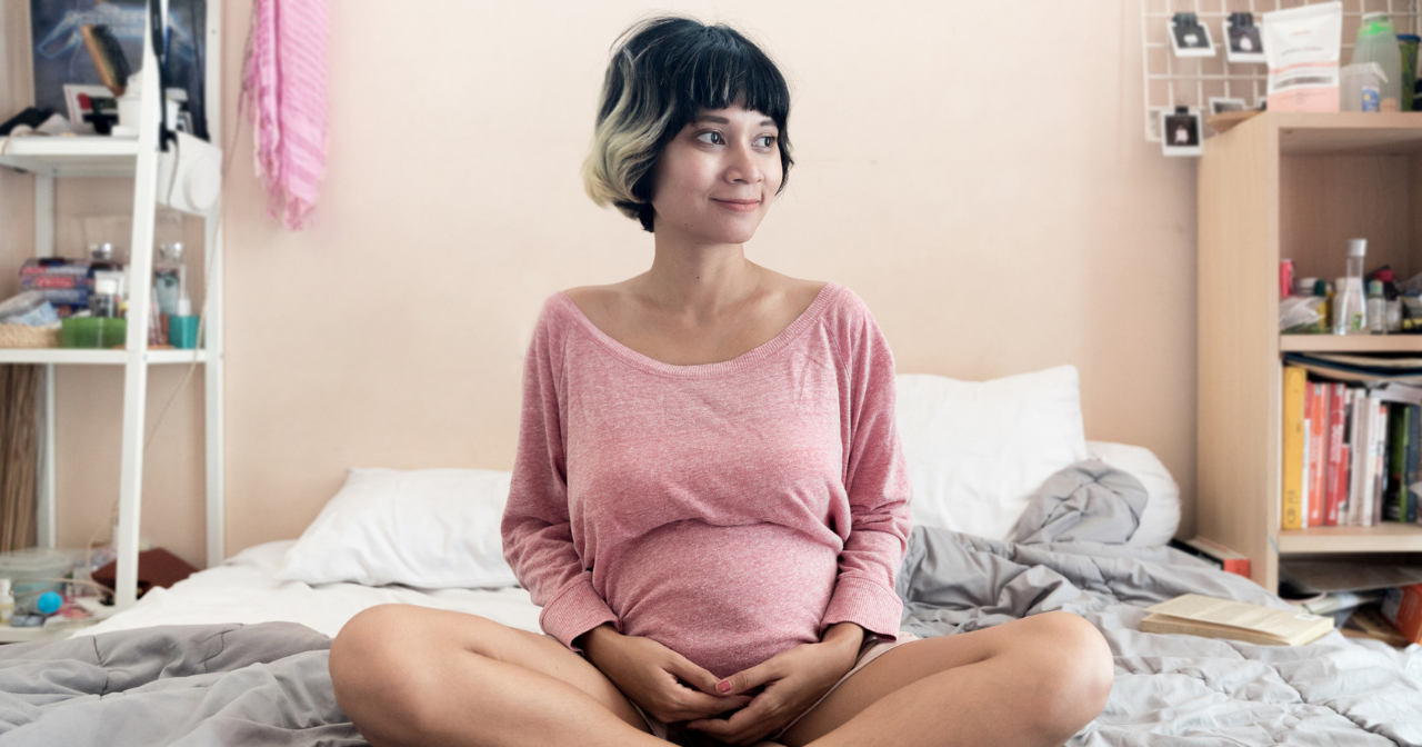 A pregnant woman sits cross legged on a bed