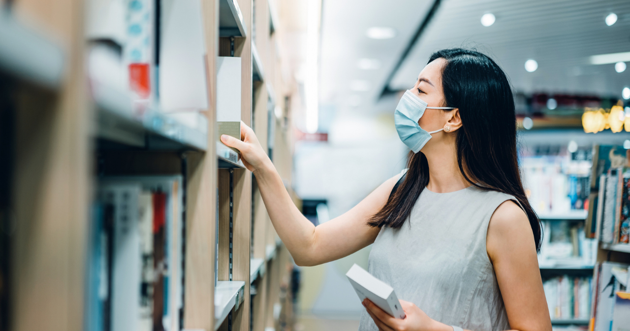 A woman wearing a mask browses books at a library. 