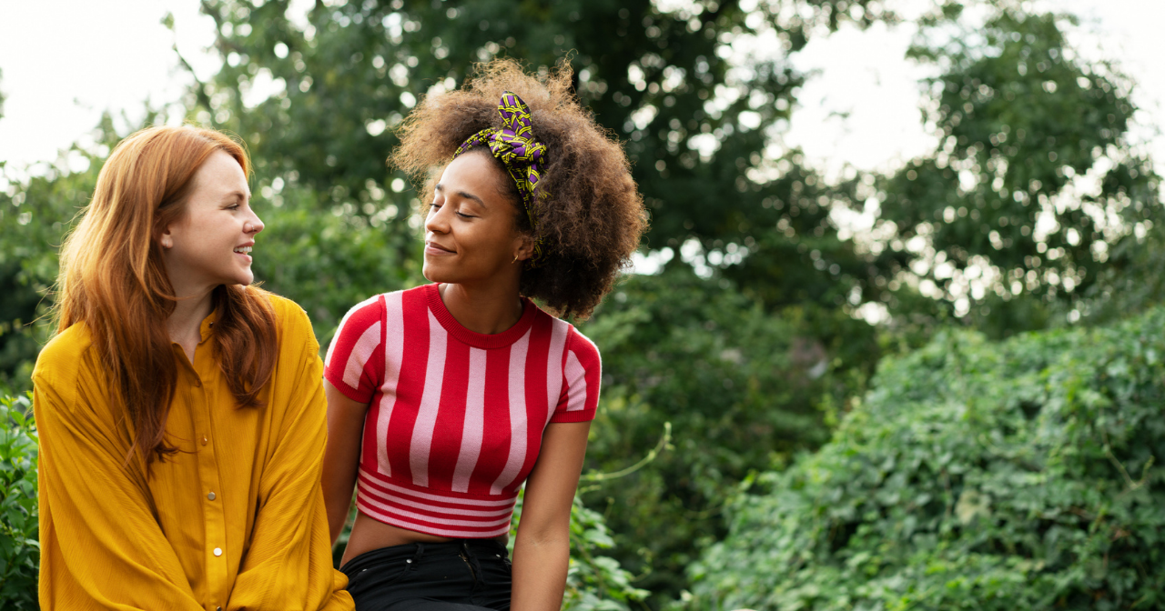 Two friends sit on a wall next to one another and share a smile. 