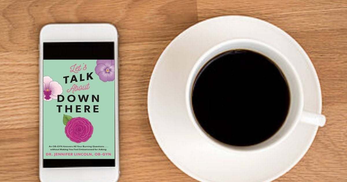 An image of a phone and a cup of coffee on a table. The cover of the book 'Let's Talk About Down There' is on the phone. 