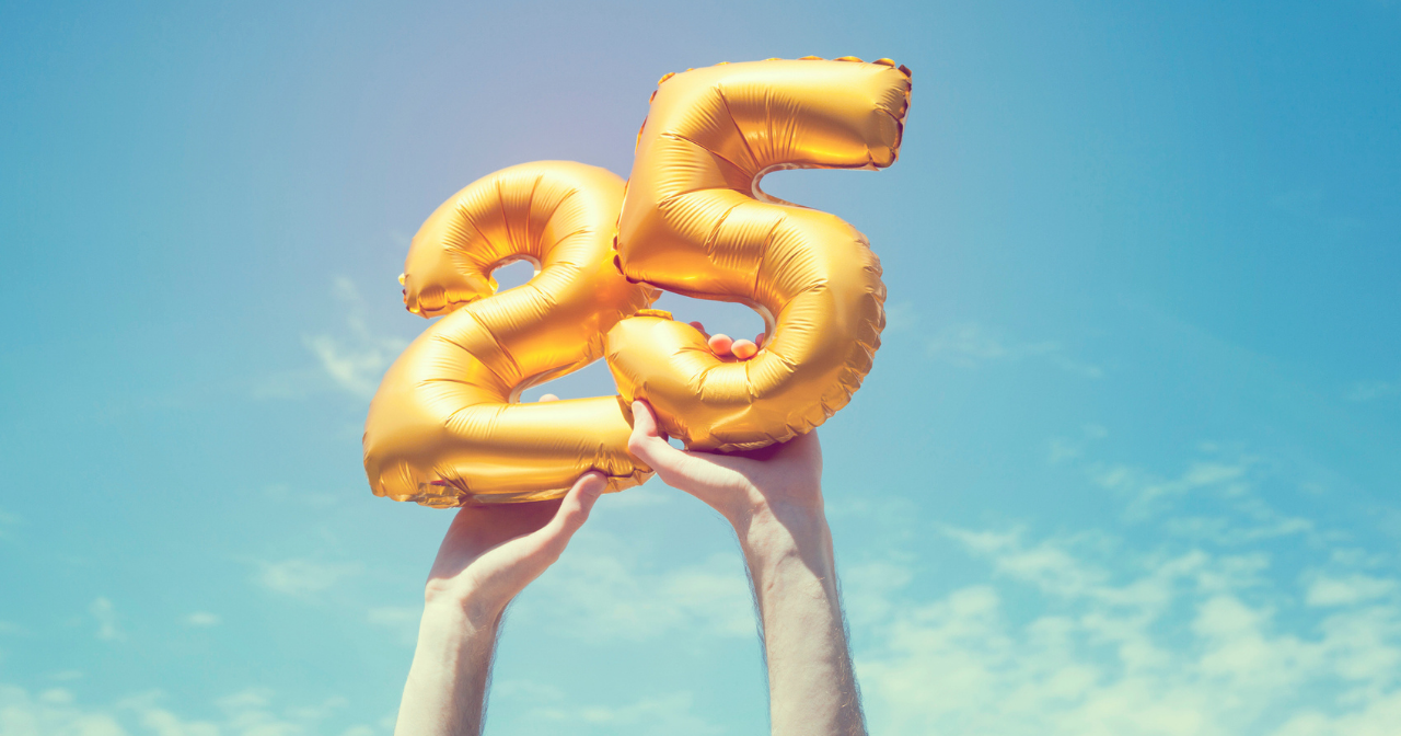 Hands hold golden balloons with the numbers 2 and 5 up to the sky. 