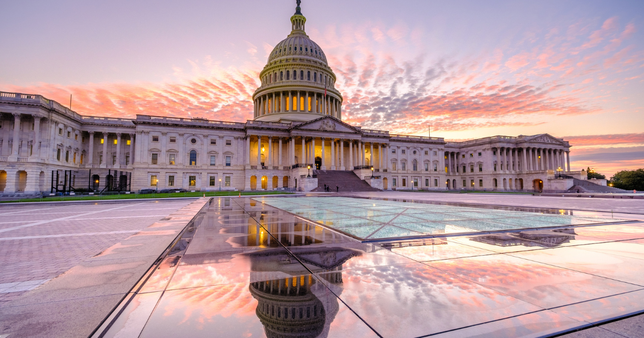 An image of the US Capitol building from the outside with a pink and purple sunset in the background.