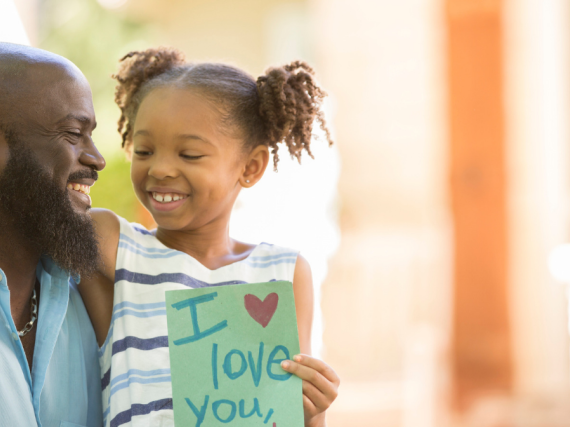 a young girl sits on her father's lap with a card that says, "I love you, dad."