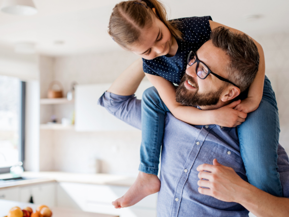 A young girl sits on her father's shoulders inside a house. 