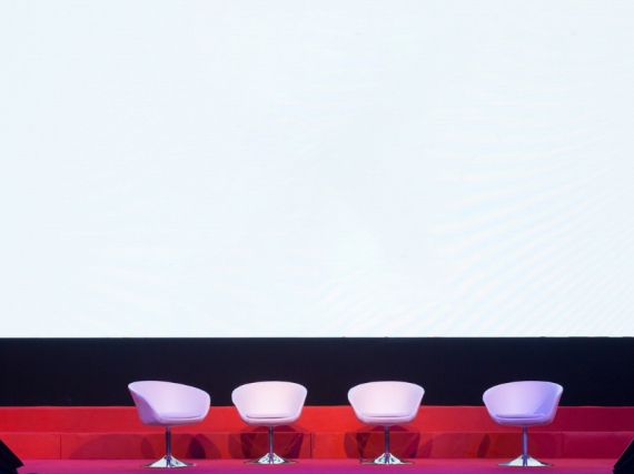 A drawing of an empty stage with four chairs set up for a panel discussion. 
