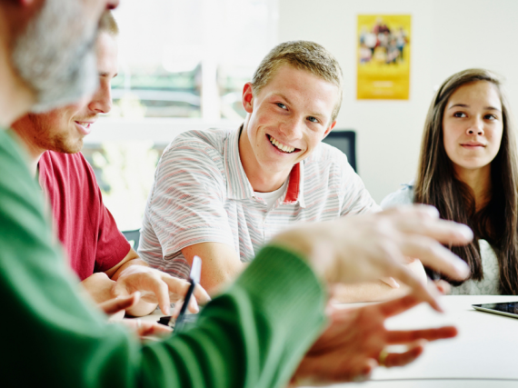 A male teacher laughs with his students as they talk together. 