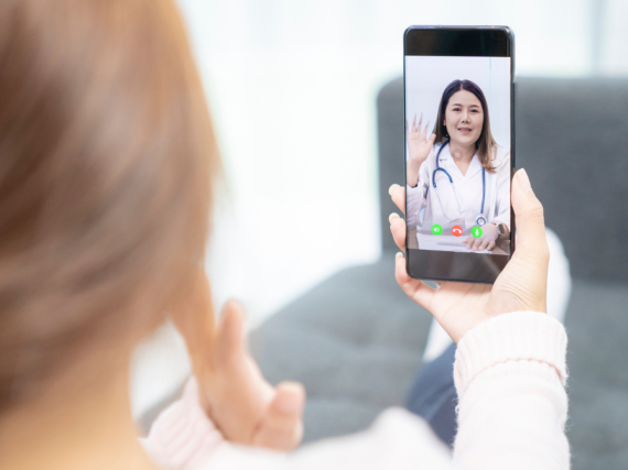 A photo of the back of a woman's head looking over her shoulder to see a health care provider on the phone in her hand. 