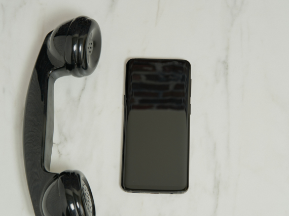 A black landline phone sits next to a black cell phone on a table.