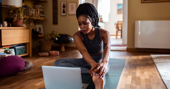 A woman stretches on a yoga mat while looking at her computer. 